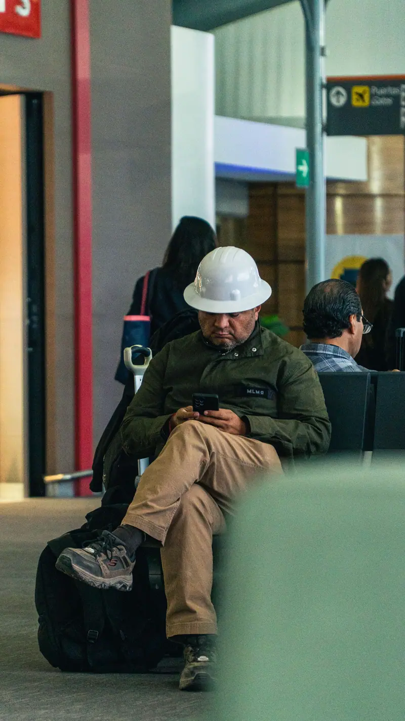 Un trabajador con casco revisa su teléfono en una sala de espera.