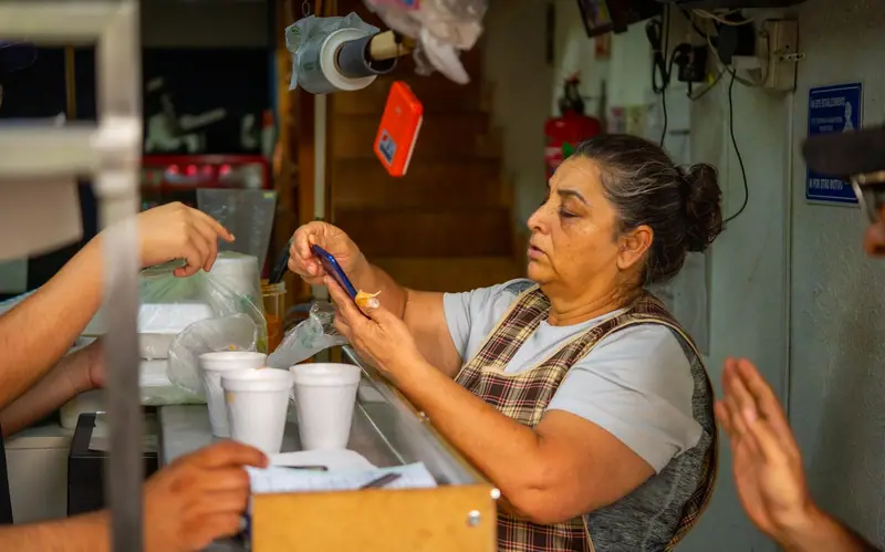 Una señora atiende su puesto de comida y revisa su teléfono.