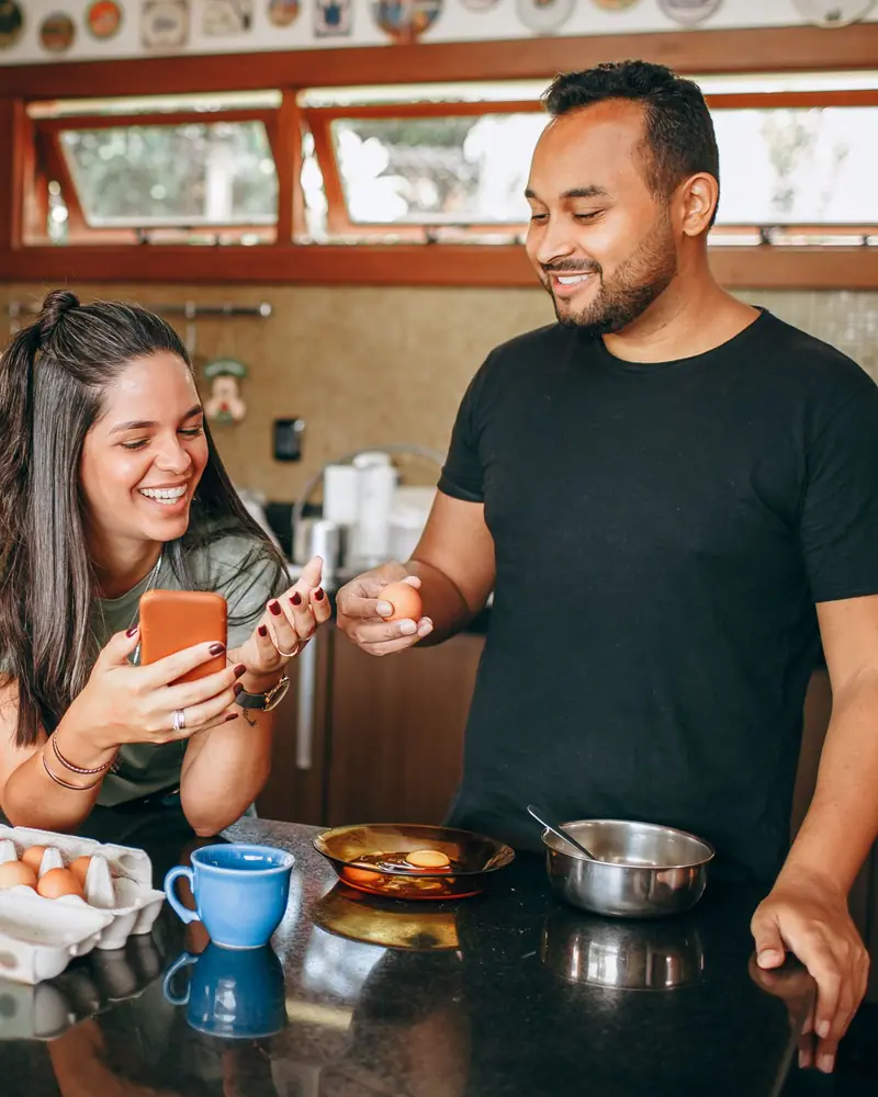 Una pareja prepara el desayuno en su cocina; ella revisa su teléfono.